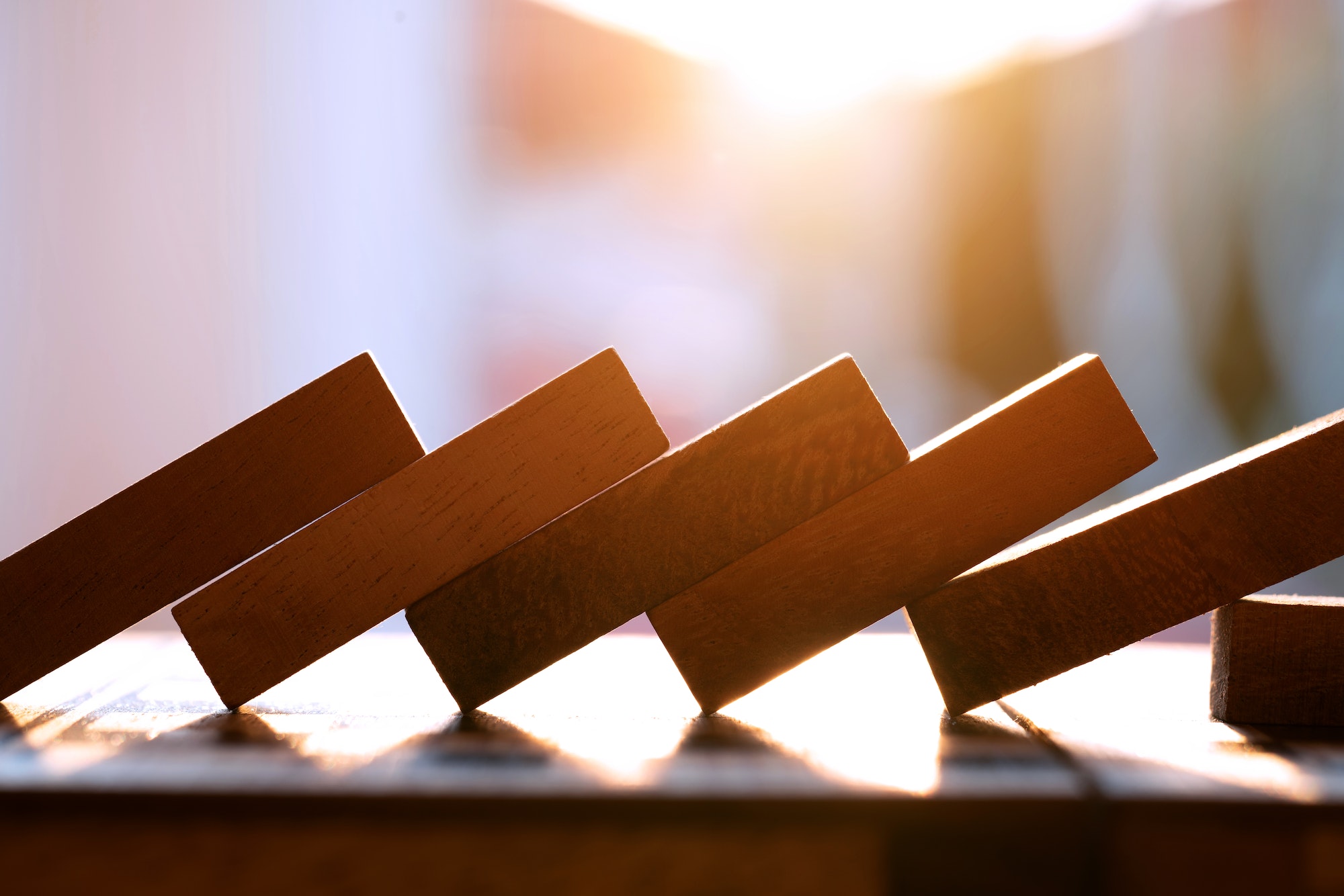 Business loss and falling concept. Block wooden game domino effect under sunset background.